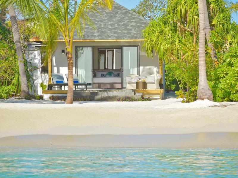 Villa sulla spiaggia con palme, sabbia e vista sull'acqua limpida del mare.