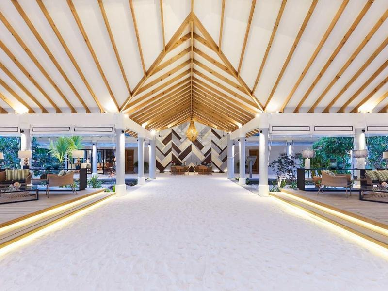 Moderna hall d'albergo aperta con travi di legno alte, aree salotto confortevoli e pavimentazione luminosa.