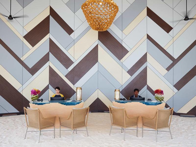 Area lounge moderna dell'hotel con parete geometrica, lampade intrecciate e comode poltrone.