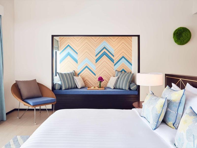 Camera d'hotel moderna con letto grande, zona salotto e specchio decorativo.