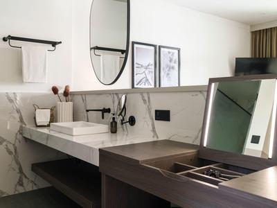 Moderner Badezimmerbereich mit Waschbecken, rundem Spiegel und grauer Marmorwand.