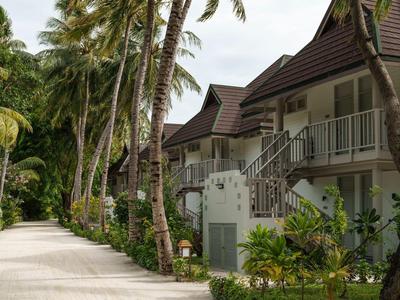 Weg entlang tropischer Palmen zu Bungalows mit Balustraden und Stufen.