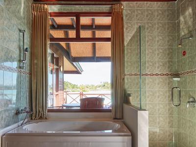Badewanne mit Blick auf Terrasse und Landschaft durch großes Fenster.
