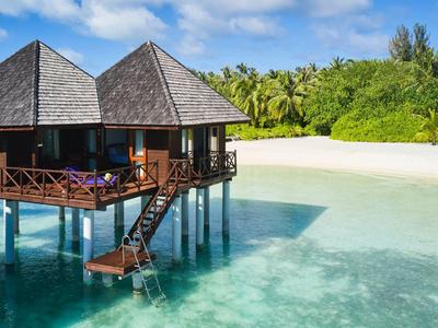 Überwassertherme mit Holzsteg über klarem türkisfarbenem Wasser an weißem Sandstrand.