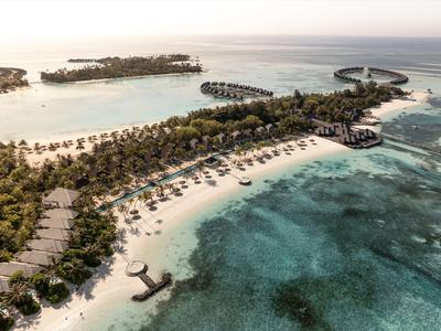 Luftaufnahme einer tropischen Insel mit Strand, Palmen und Villen im türkisfarbenen Meer.