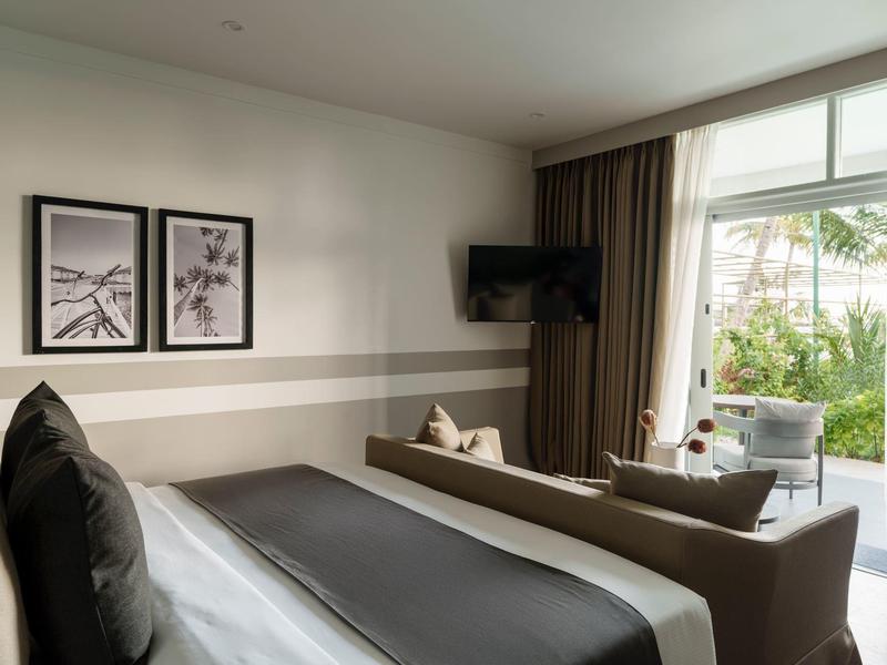 Camera d'hotel moderna con letto, divano, TV e grande finestra con vista sul verde.