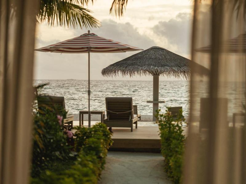 Vista attraverso tende aperte su sdraio e ombrelloni sulla spiaggia al tramonto.