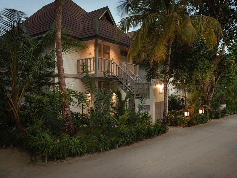 Una casa su due piani con veranda circondata da palme al crepuscolo.