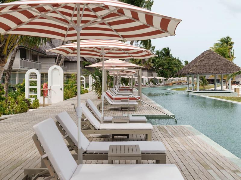 Lettini con ombrelloni a strisce accanto a una piscina su un pontile in legno.