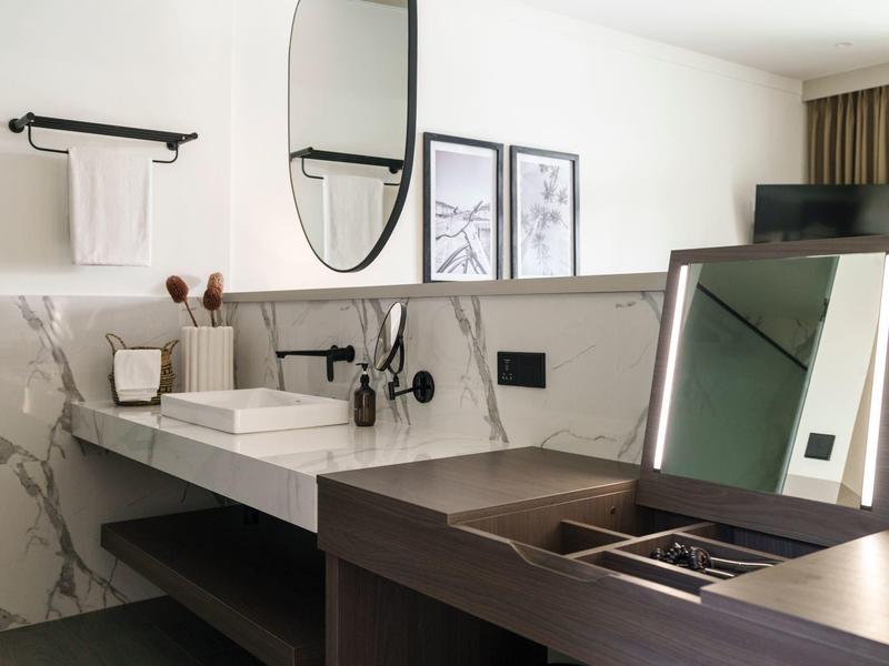 Area bagno moderna con lavabo, specchio rotondo e parete in marmo grigio.