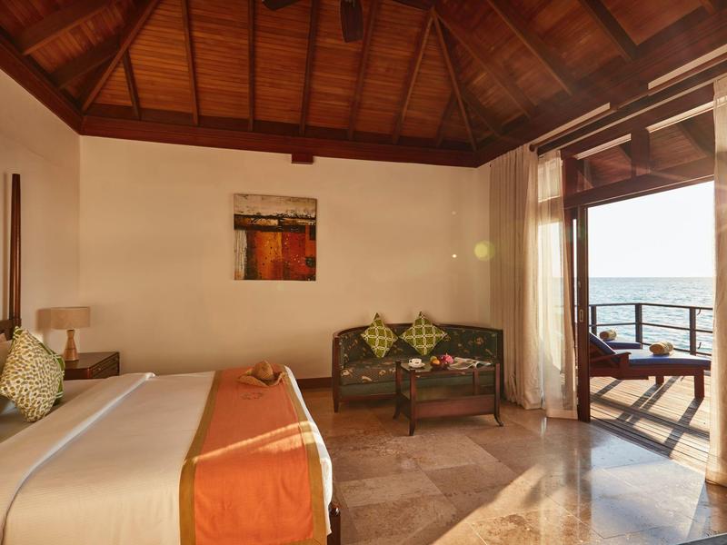 Camera d'hotel accogliente con soffitto con travi in legno, divano, letto e balcone con vista mare.