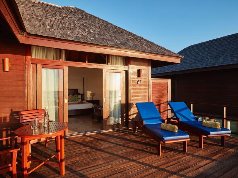 Terrazza con mobili in legno e sdraio blu in una baita accogliente sotto un cielo limpido.