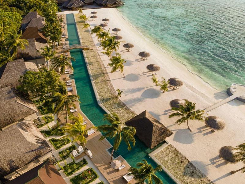 Resort sulla spiaggia con piscine, palme e mare turchese in una giornata di sole.