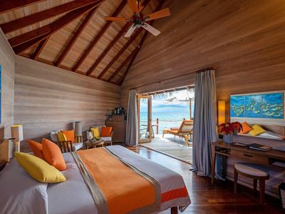 Gemütliches Hotelzimmer mit Holzdecke, Bett mit orangefarbenen Akzenten und Meerblick durch große Tür