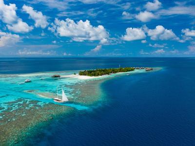 Kleine Insel mit weißem Segelboot in klarem, blauem und türkisfarbenem Wasser unter blauem Himmel.