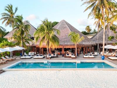 Luxuriöse Poolanlage vor einem tropischen Hotel mit Palmen und weißen Sonnenschirmen.