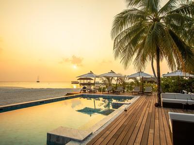 Poolbereich mit Blick auf das Meer bei Sonnenuntergang und Palmen am Strand.