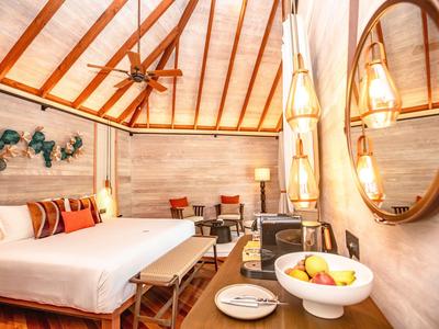 Helles, gemütliches Hotelzimmer mit Holzbalkendecke, Doppelbett, Sitzbereich und Obstschale.