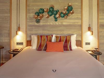 Modernes Schlafzimmer mit großem Bett, dekorativen Kissen und hellen Hängelampen an einer Holzwand.