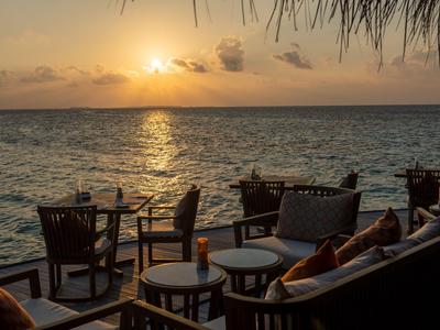 Außenbereich mit Sitzgelegenheiten am Wasser bei Sonnenuntergang mit orangefarbenem Himmel.