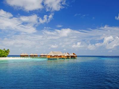 Bungalows über klarem, blauem Wasser mit strahlend blauem Himmel und weißen Wolken.