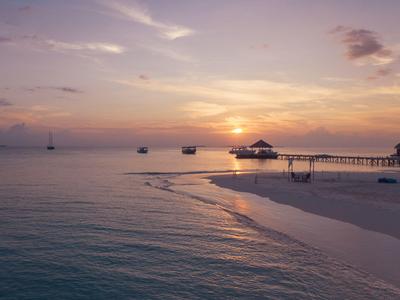 Sonnenuntergang über ruhigem Meer mit Strand und Steg im Urlaubsort.