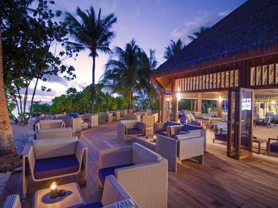 Gemütliche Außenlounge mit Sesseln und Tischen, Palmen am Strand bei Abenddämmerung.