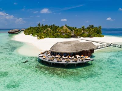 Ein Hotelresort auf einer Insel mit klarem Wasser, Sandstrand und einem runden Restaurant am Steg.