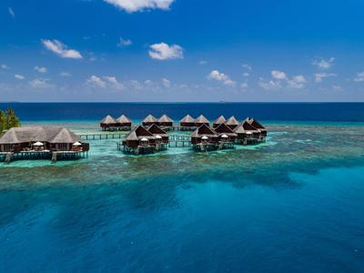 Bungalows auf Stelzen über klarem türkisfarbenem Wasser unter blauem Himmel im tropischen Urlaubsparadies.