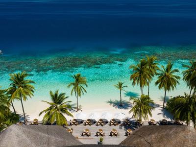 Strand mit weißen Sand, Palmen und blauem Meer, Sonnenschirme in Hotelnähe.