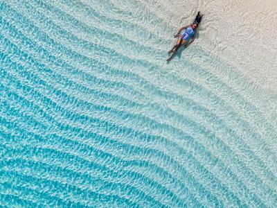 Eine Person schwimmt im klaren, türkisfarbenen Wasser knapp vor einem sandigen Strand.