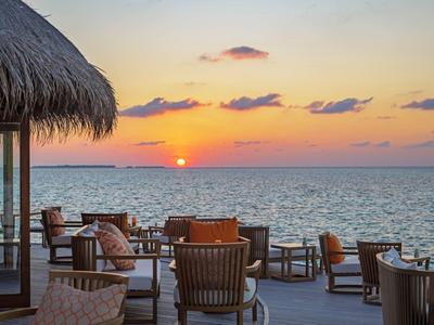 Terrasse mit Stühlen und Tischen am Meer bei Sonnenuntergang