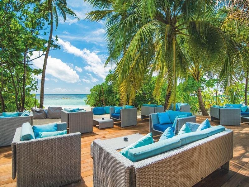 Lounge-Bereich mit Sitzmöbeln und Kissen unter Palmen mit Blick auf das Meer.