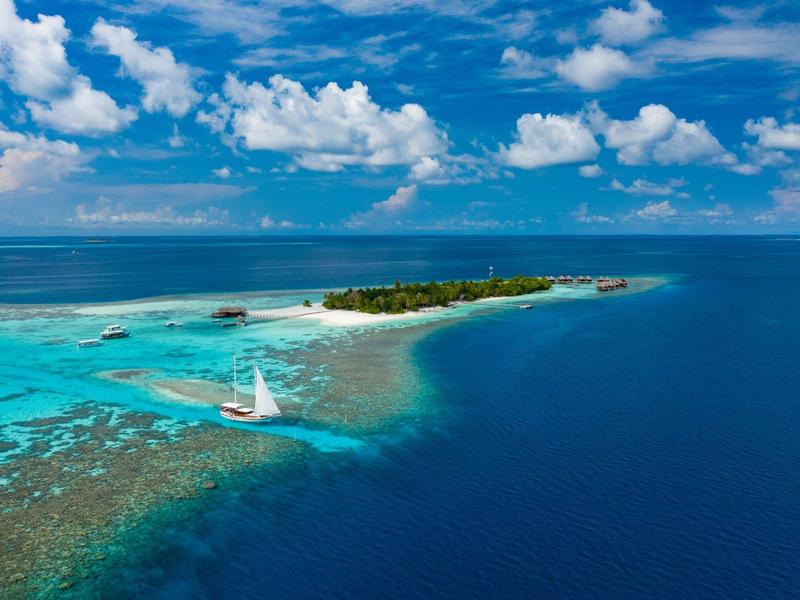 Kleine Insel mit klarem türkisfarbenem Wasser und Segelboot unter hellem Himmel.