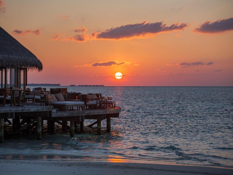 Sonnenuntergang über dem Meer mit einem Steg und Liegestühlen am Strand