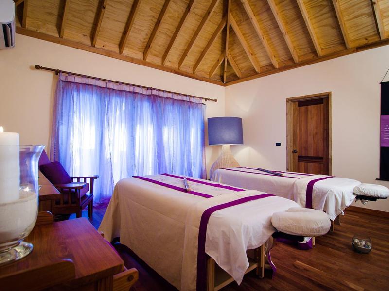 Zimmer mit zwei Massageliegen, Holzboden und Decke, weichen Vorhängen und entspannter Atmosphäre