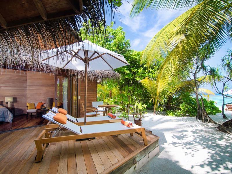 Strandresort mit Liegen unter einem Sonnenschirm, Palmen und Blick auf das Meer