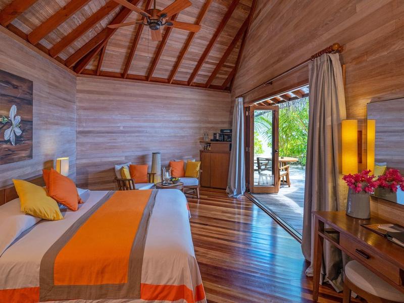 Modernes Holzbungalow-Zimmer mit Bett, Schreibtisch und offener Tür zum Garten