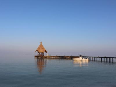 Eine kleine hölzerne Kapelle am Steg, ruhig umgeben von blauem Wasser und klarem Himmel.