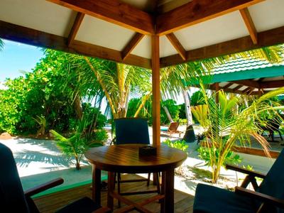 Überdachte Terrasse mit Holzmöbeln, grünen Pflanzen und Blick auf einen Garten bei Sonnenschein.