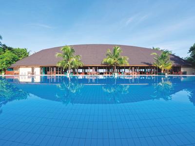 Großer Pool mit klarem Wasser vor rundem Gebäude und Palmen, blauer Himmel im Hintergrund.
