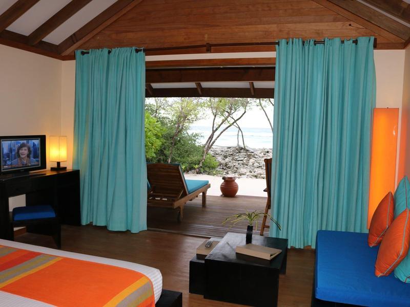 Gemütliches Zimmer mit türkisfarbenen Vorhängen, orangem Bett und blauem Sofa am offenen Balkon.