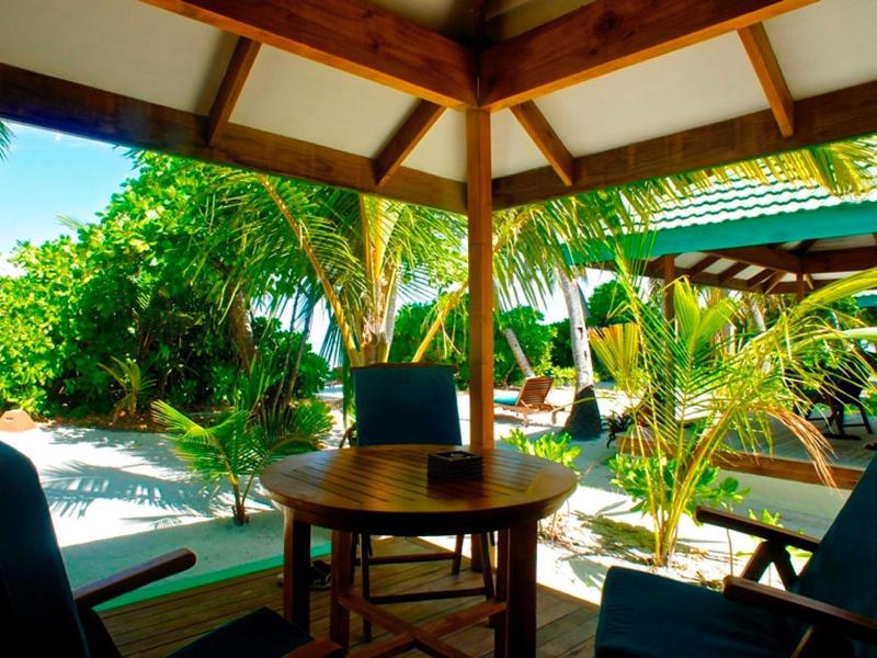 Überdachte Terrasse mit Holzmöbeln, grünen Pflanzen und Blick auf einen Garten bei Sonnenschein.