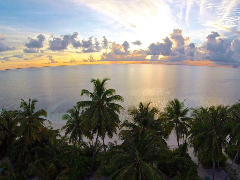 Strand mit Palmen am Meer bei Sonnenuntergang, bunte Wolken am Himmel und ruhiges Wasser.