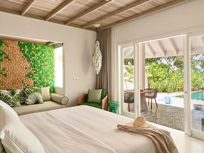 Helles Hotelzimmer mit Holzdecke, Begrünungswand und Terrassentür zum Poolbereich.