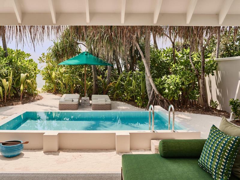 Moderner Poolbereich mit Liegestühlen und grünem Sonnenschirm in tropischer Umgebung.