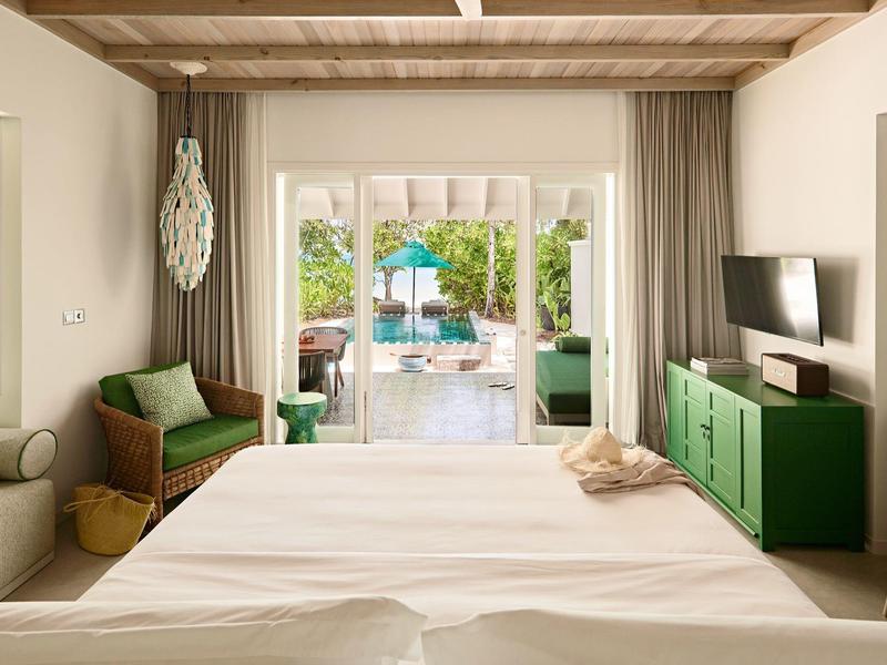 Gemütliches Hotelzimmer mit Blick auf einen Pool und Garten durch eine Glasschiebetür.