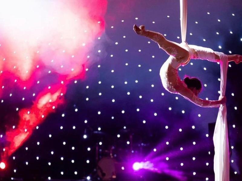 Akrobat performt an Tüchern vor buntem Bühnenlicht.