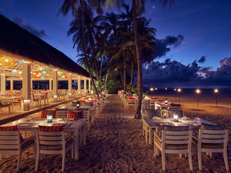 Abendliche Strandrestaurant mit gedeckten Tischen unter Palmen und leuchtendem Himmel.