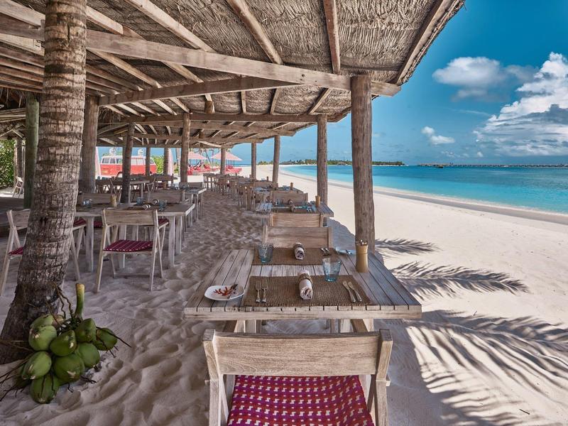 Offenes Strandrestaurant mit Holzmöbeln und Blick auf den weißen Sandstrand und das Meer.